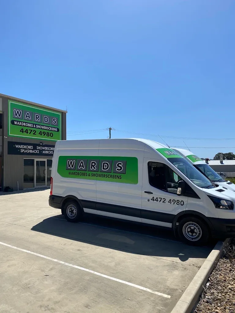 A white Wards Wardrobes & Showerscreens van parked in front of the Wards workshop on Cranbrook Road, Batemans Bay, with a second van behind it and the green Wards sign